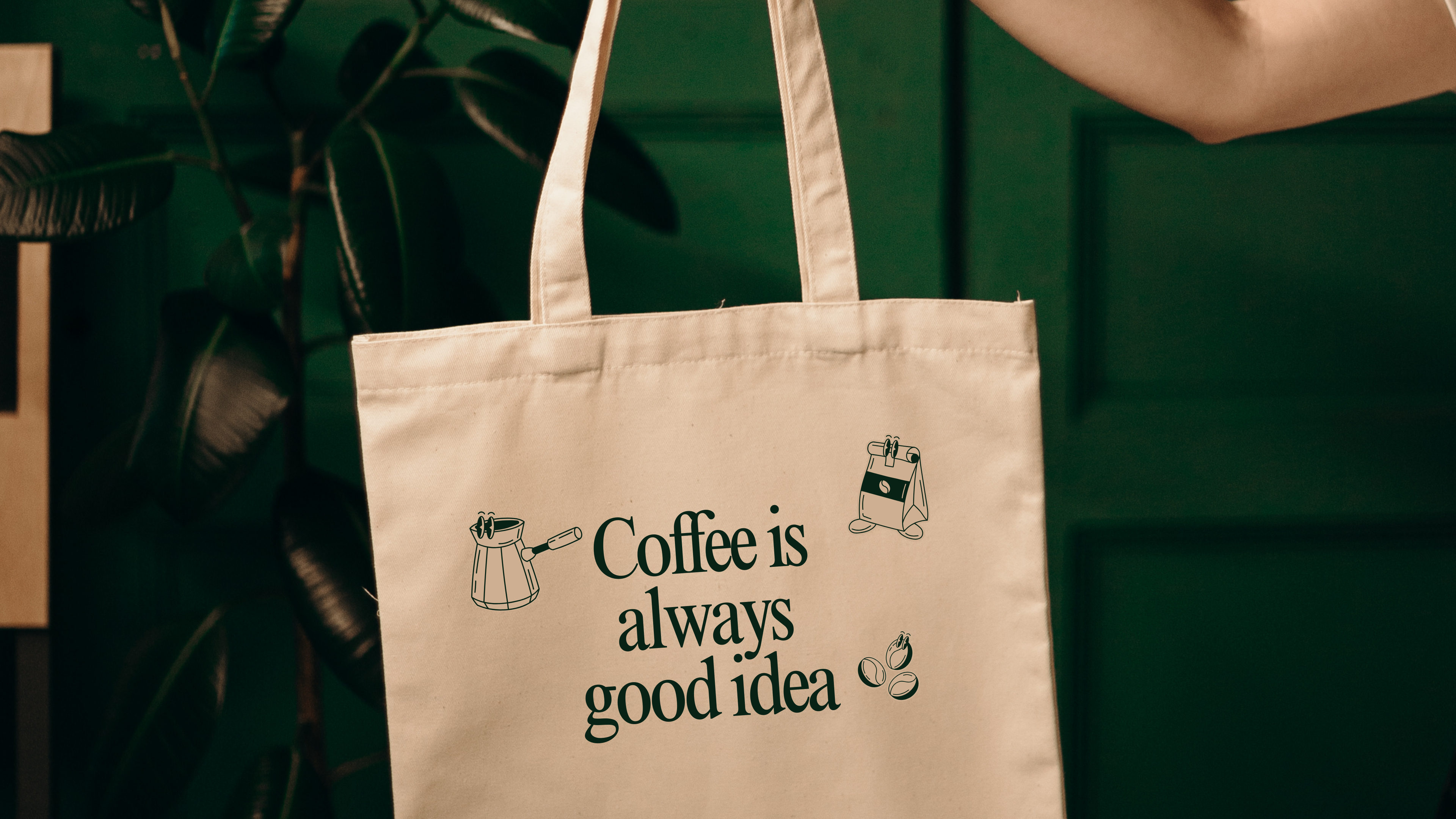 Image of a hand holding a tote bag that says " Coffee is always a good idea"